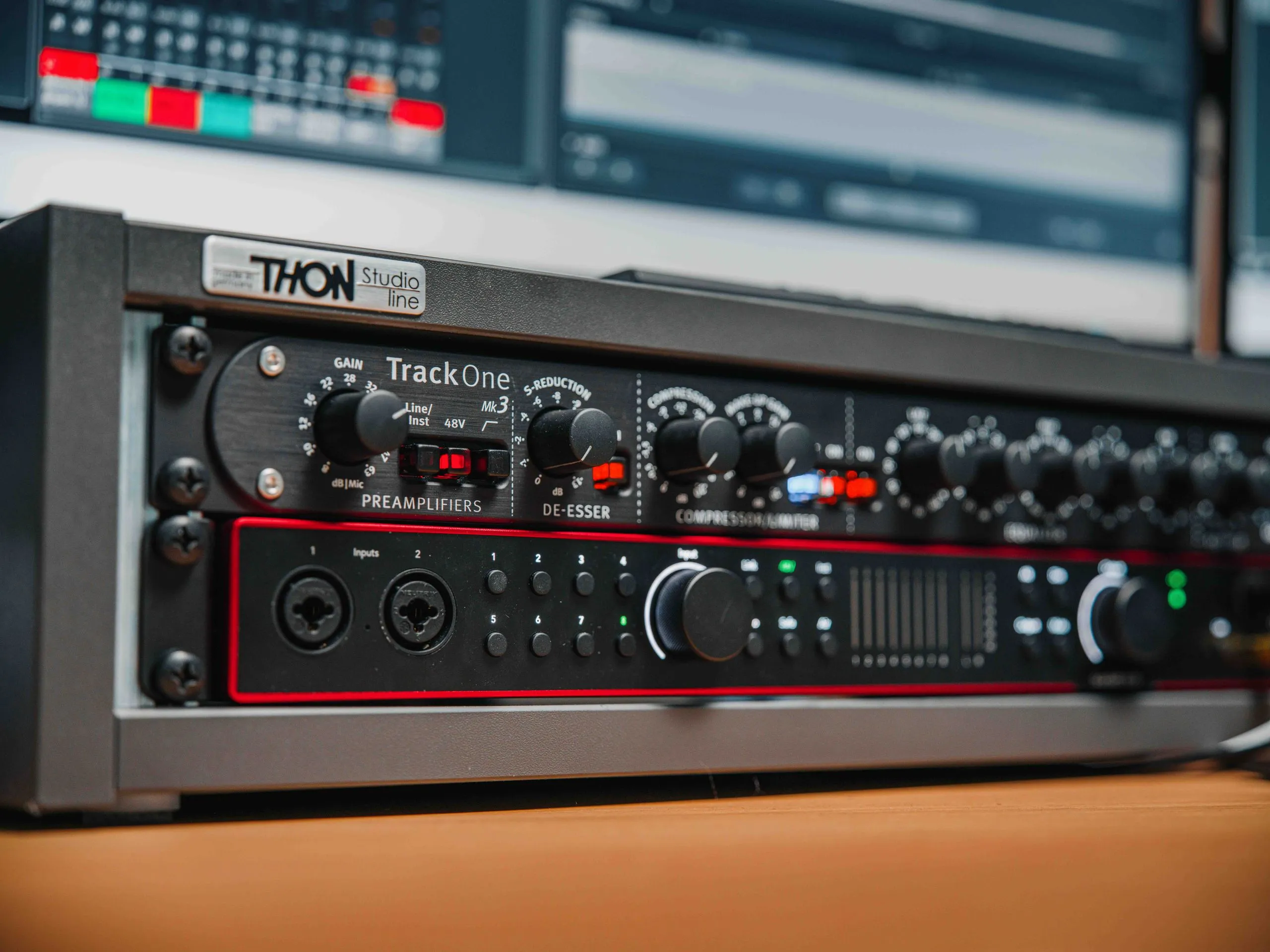 Zwei Rack-Einheiten, eine THON Studio Line TrackOne mit Gain-Reglern und Schaltern und eine zweite Einheit mit Eingangsanschlüssen und weiteren Reglern, stehen nebeneinander auf einem Holztisch, mit einem Computerbildschirm im Hintergrund.
